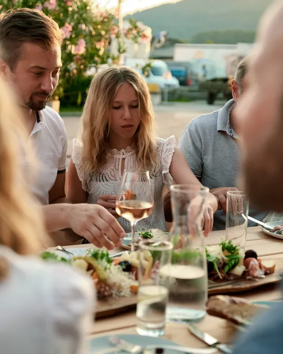 Freunde genießen ein Abendessen im Freien mit Wein und frischen Salaten an einem sonnigen Abend